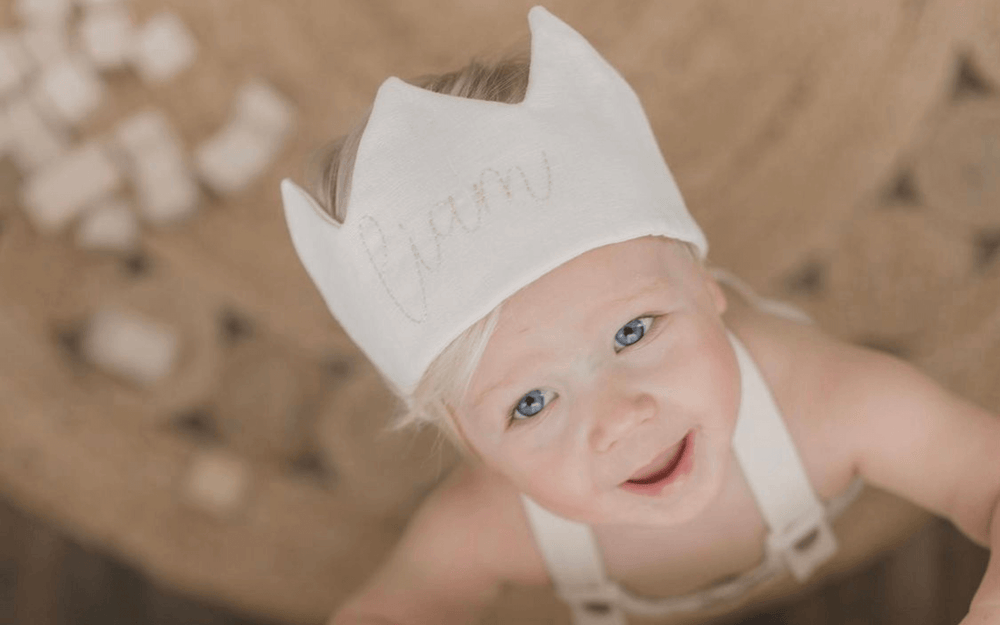 little boy wearing a linen waldorf birthday crown with his name on it and he is playing with wooden blocks