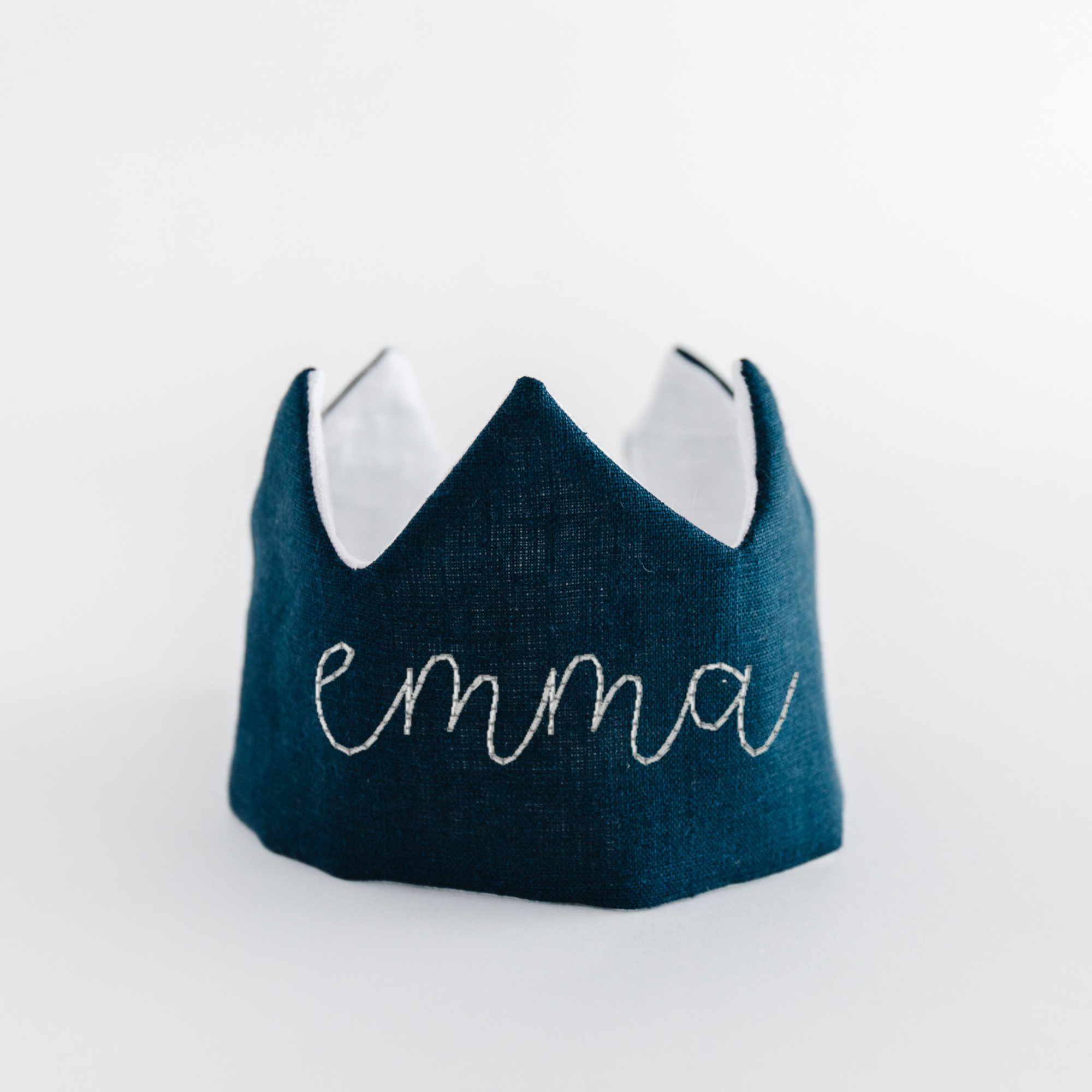 Flat lay of navy blue linen crown with name 'Emma' embroidered in white thread