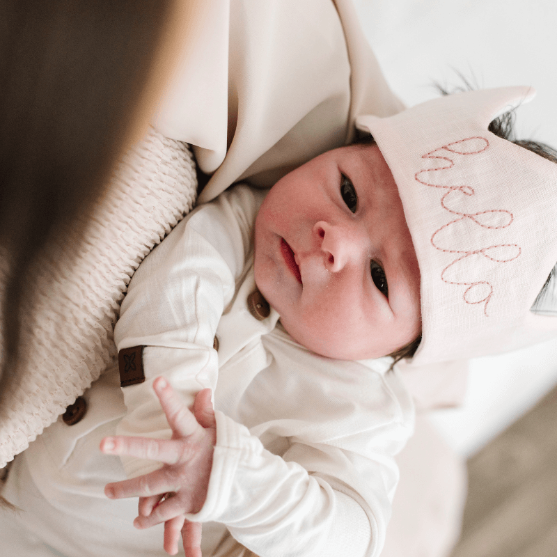 Newborn baby girl wearing a pink crown embroidered with the word 'hello'.