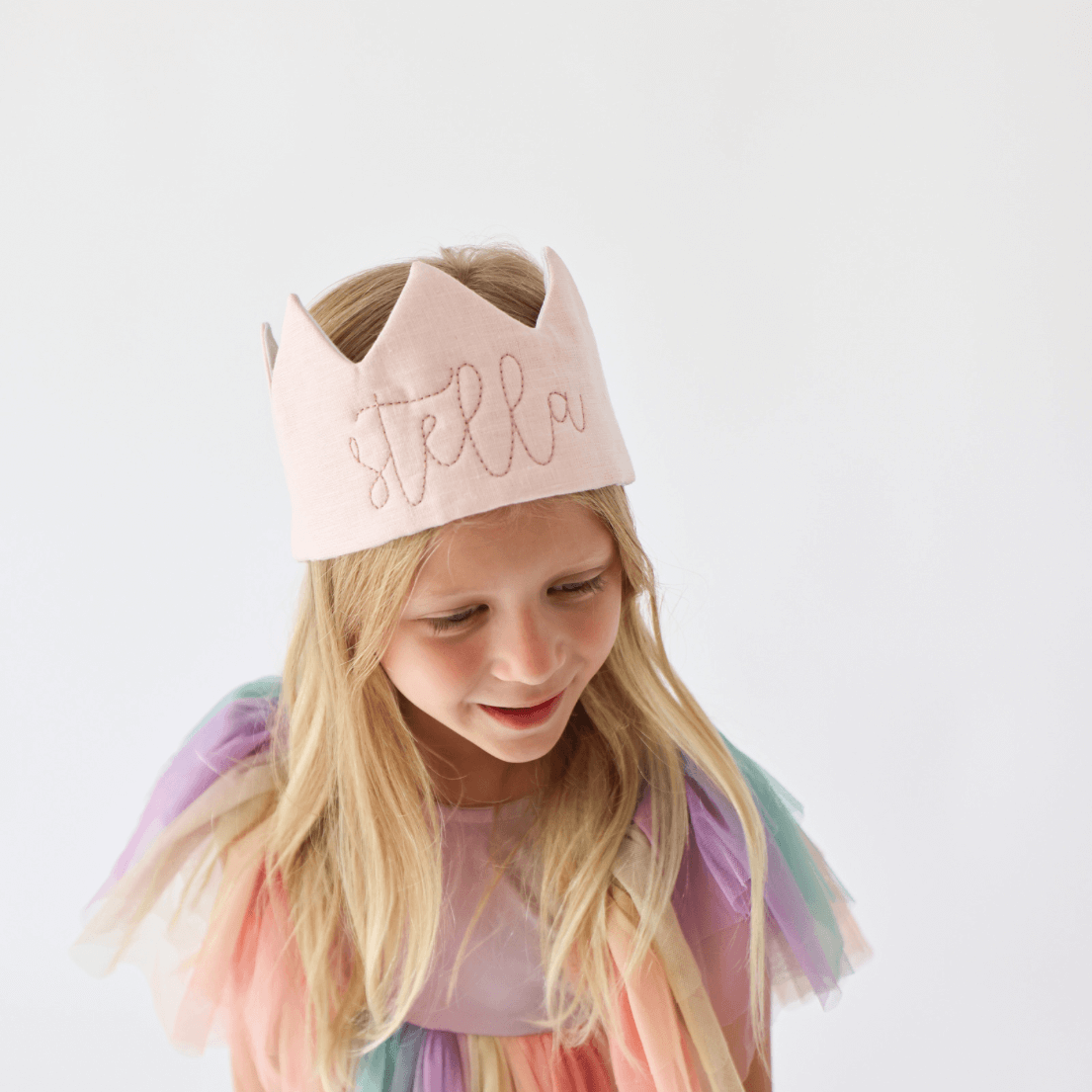 Blonde girl in rainbow dress wearing pink birthday crown with name embroidered