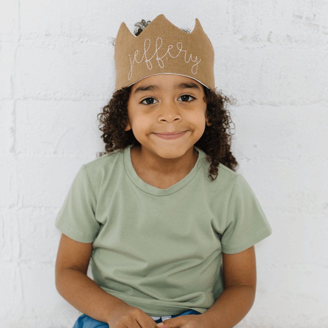 Smiling boy wearing camel brown crown with name 'Jeffrey' embroidered in white thread
