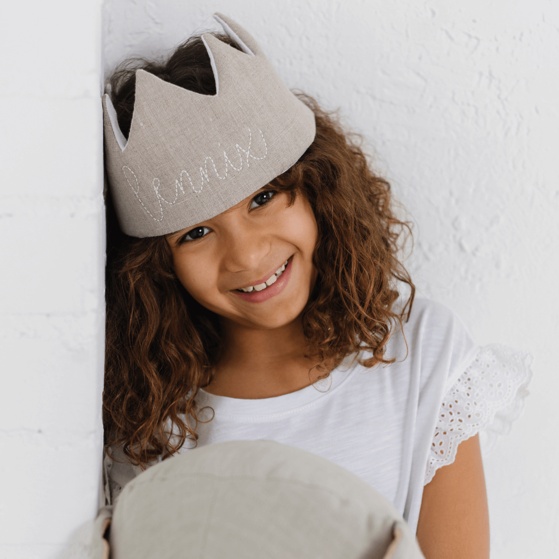Smiling girl with dark curly hair wearing a taupe linen birthday crown with her name on it