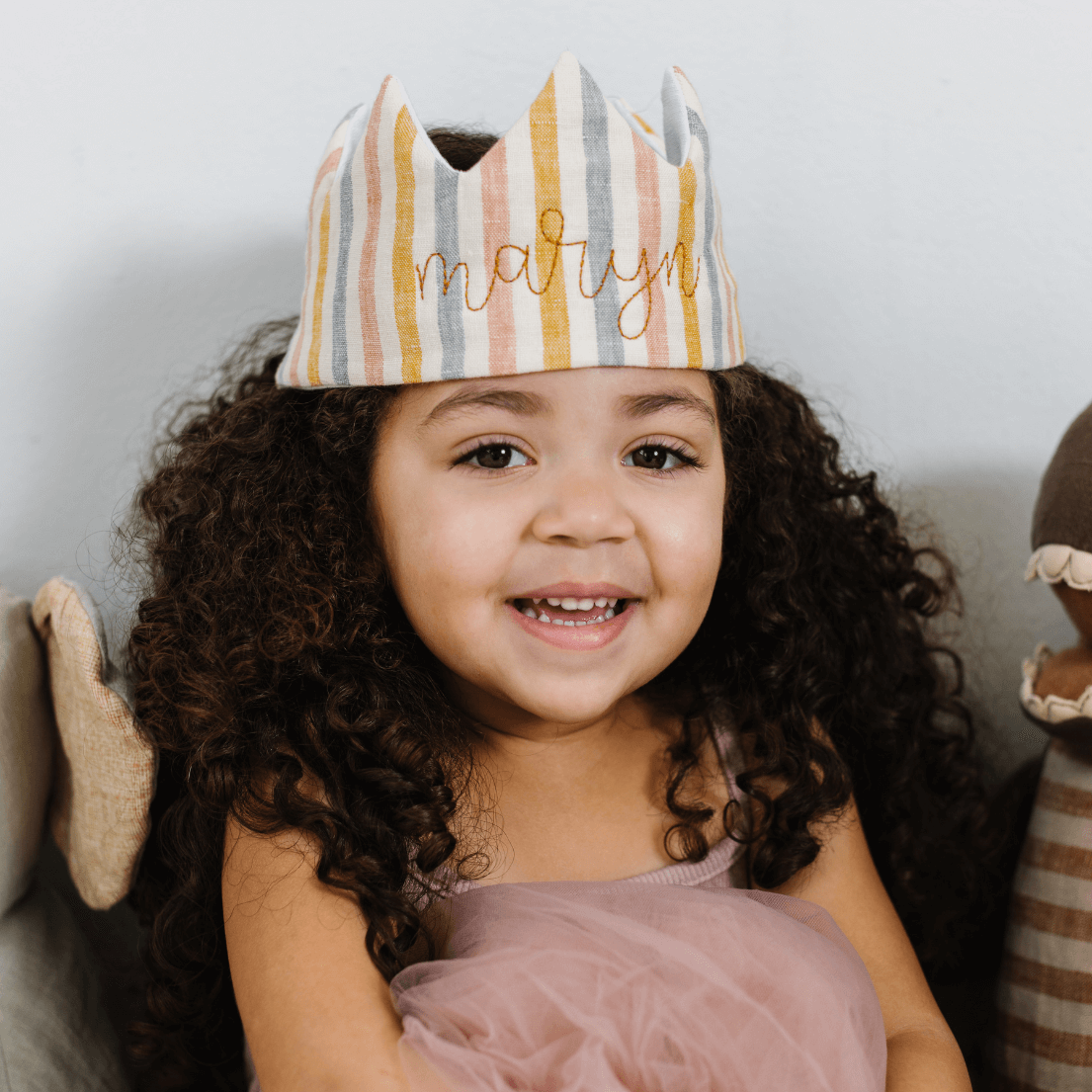 Girl in a pink dress wearing striped linen birthday crown with gold embroidery