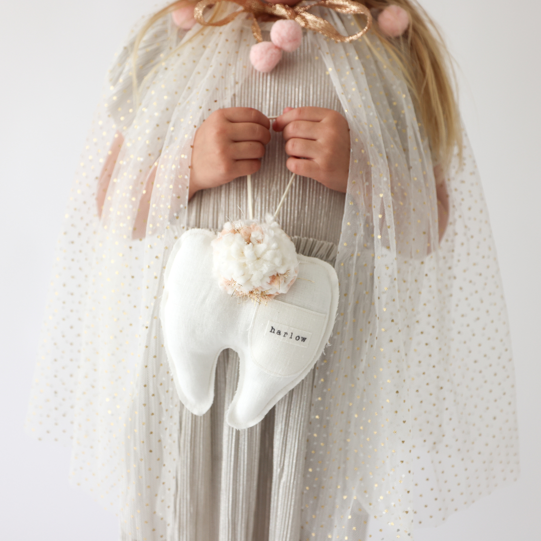 Child in a tulle dress holding white tooth fairy pillow with pom pom detail