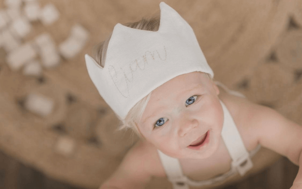 little boy wearing a linen waldorf birthday crown with his name on it and he is playing with wooden blocks