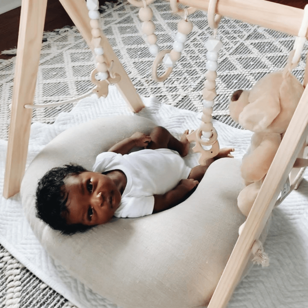 newborn baby laying on boppy pillow under a play gym