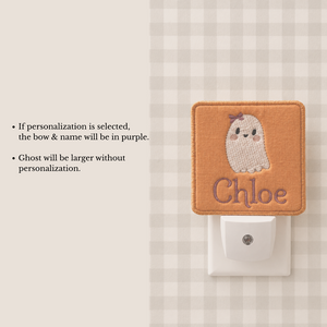A personalized orange fabric night light plug-in featuring an embroidered cute ghost with a purple bow and the name 'Chloe' in purple. The image includes text explaining that the bow and name will be in purple if personalization is selected.
