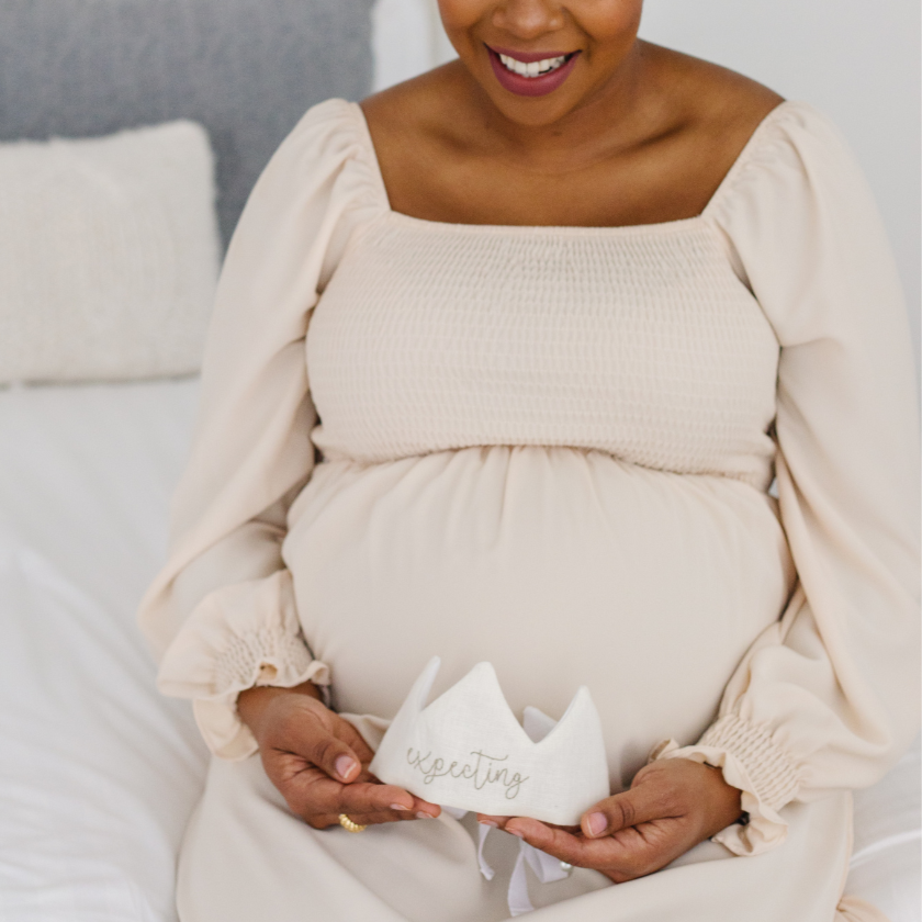 PREGNANT WOMAN HOLDING A CROWN THAT IS EMBROIDERED WITH EXPECTING