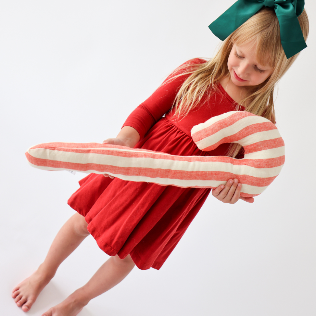 little girl in red dress holding a giant candy cane pillow