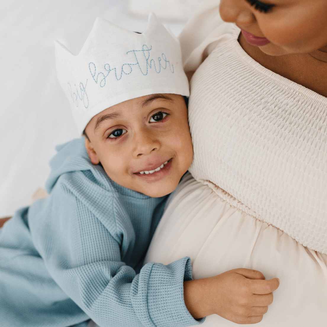 little boy cuddling with mom and wearing a big brother crown